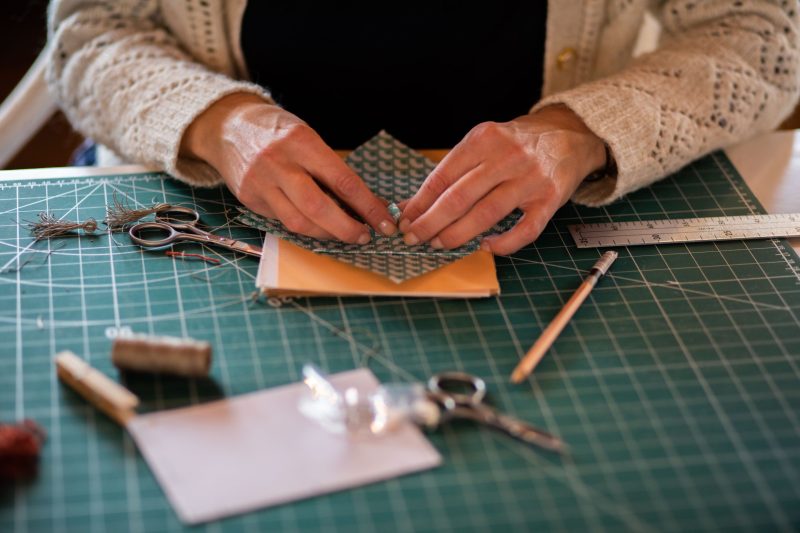 A pair of hands are folding up colourful card at a craft table.