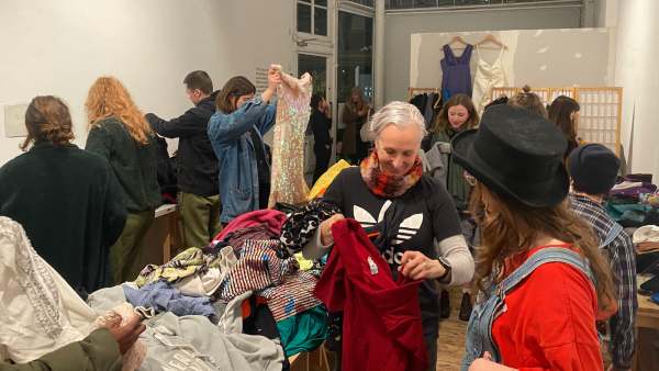 An image of ONCA clothes swap. People are looking through piles of clothes and chatting.